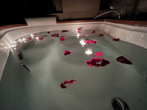 A bathtub with rose petals and candles.