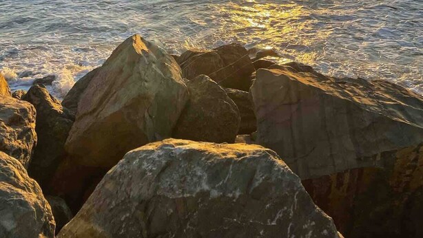 A sunset over a calm sea with rocks in the foreground.