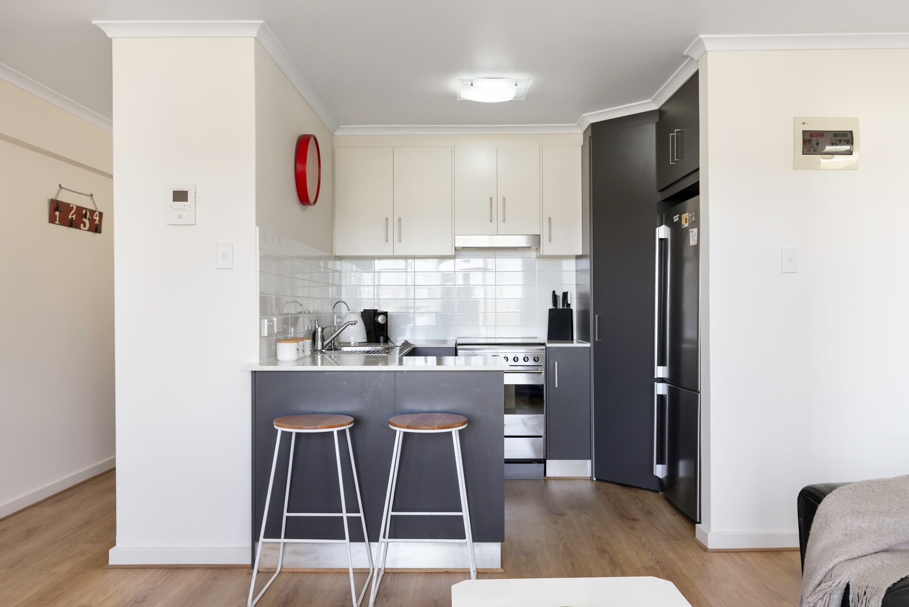 A modern kitchen with white cabinets, a central island with stools, a stainless steel refrigerator, and a built-in oven.