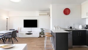 A modern kitchen with a flat-screen TV, a red clock, and a dining area with a table and chairs.