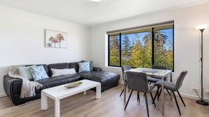 A modern living room with a black leather sofa, white coffee table, and a dining area with a glass table and chairs.
