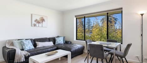 Ein modernes Wohnzimmer mit einem schwarzen Ledersofa, einem weißen Couchtisch und einem Essbereich mit einem Glastisch und Stühlen.