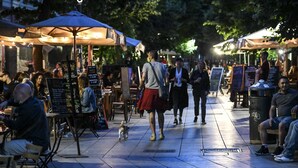 Un mercato all'aperto con tavoli e ombrelloni, persone che passeggiano e un cane al guinzaglio.