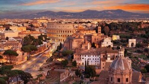 Una vista panoramica di una città storica con un'architettura antica imponente, tra cui un grande colosseo ed edifici classici.