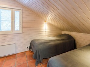 Un dormitorio pequeño, con un solo cuarto, en el ático, con techo inclinado, una ventana con persianas, una lámpara de pared y un radiador.