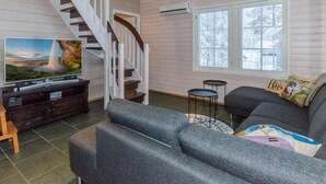 Un salon avec un escalier, une télévision, un canapé et une fenêtre donnant sur des arbres.