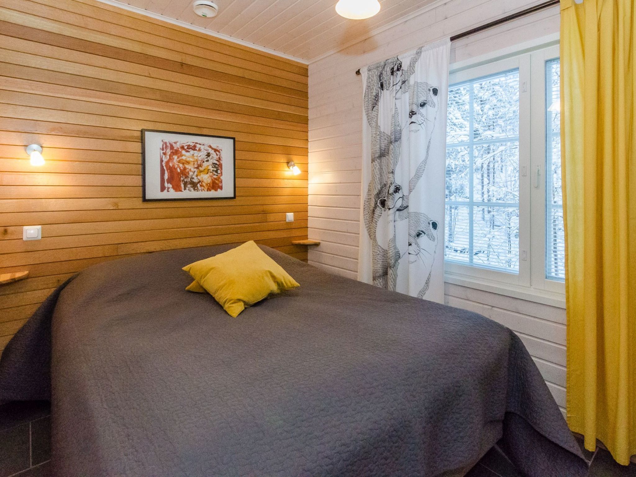 A room with a bed, a window with curtains, and wall-mounted lights.