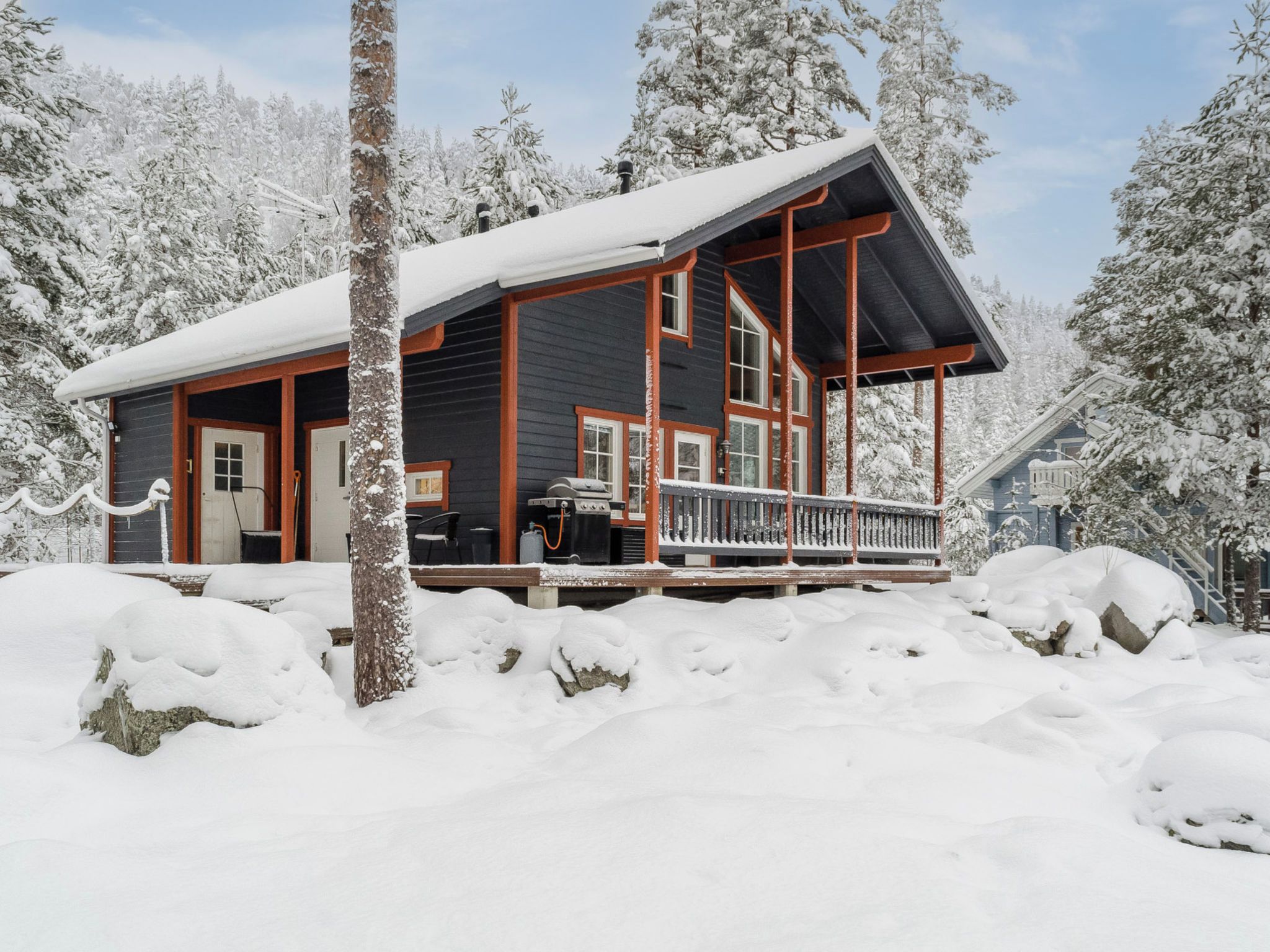 A cabin with a covered porch, a grill, and a snow-covered landscape.