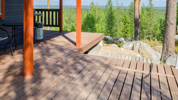 Une terrasse en bois avec une table et des chaises, donnant sur une zone boisée sous un ciel dégagé.