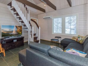 A living room with a staircase, a television, a sofa, and a window.