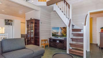 A spacious living area with a grey sofa, a wooden cabinet, a flat-screen TV, and a staircase with white railings.