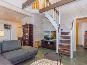 A spacious living area with a grey sofa, a wooden cabinet, a flat-screen TV, and a staircase with white railings.