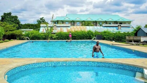 A swimming pool with a man in the water, surrounded by greenery and a building in the background. - Hotel Staridge Limited (Homa Bay)