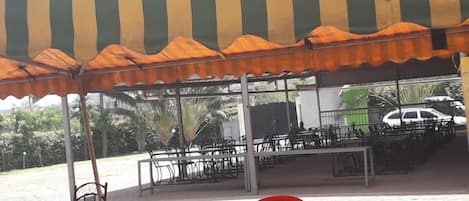 An outdoor seating area with tables and chairs under a striped awning.
