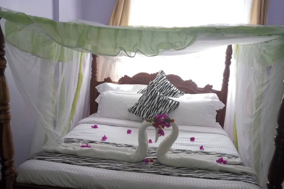 A bed with a canopy, swan-shaped pillows, and scattered flowers.