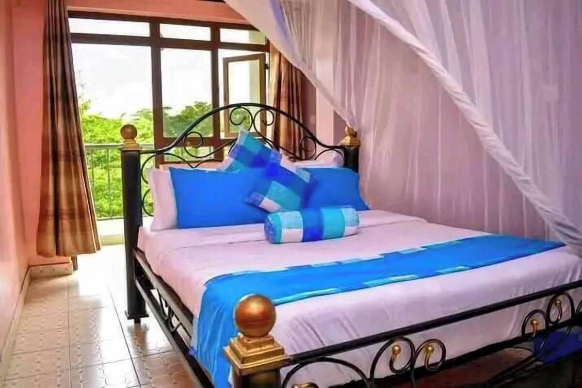 A bed with a canopy, blue bedding, and a view of greenery outside.