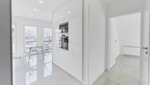 A modern kitchen with white cabinetry, a built-in oven, and a window overlooking a snowy landscape. - APARTAMENTY ŚWINOUJŚCIE - NOWA FLOTYLLA (Swinoujscie)