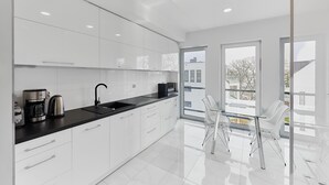 A modern kitchen with white cabinets, a black countertop, and a coffee maker. - APARTAMENTY ŚWINOUJŚCIE - NOWA FLOTYLLA (Swinoujscie)