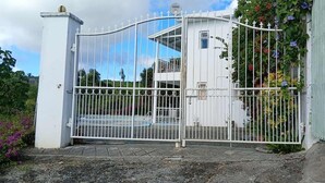 Ein von einer Mauer umgebenes Anwesen mit einem weißen Gebäude, einem Metallgitter und einem kleinen Balkon.