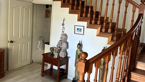 A wooden staircase with a handrail, a dining area with a round table, and a statue on a small table. - Villa les Dauphins Great for Families (La Gaulette)