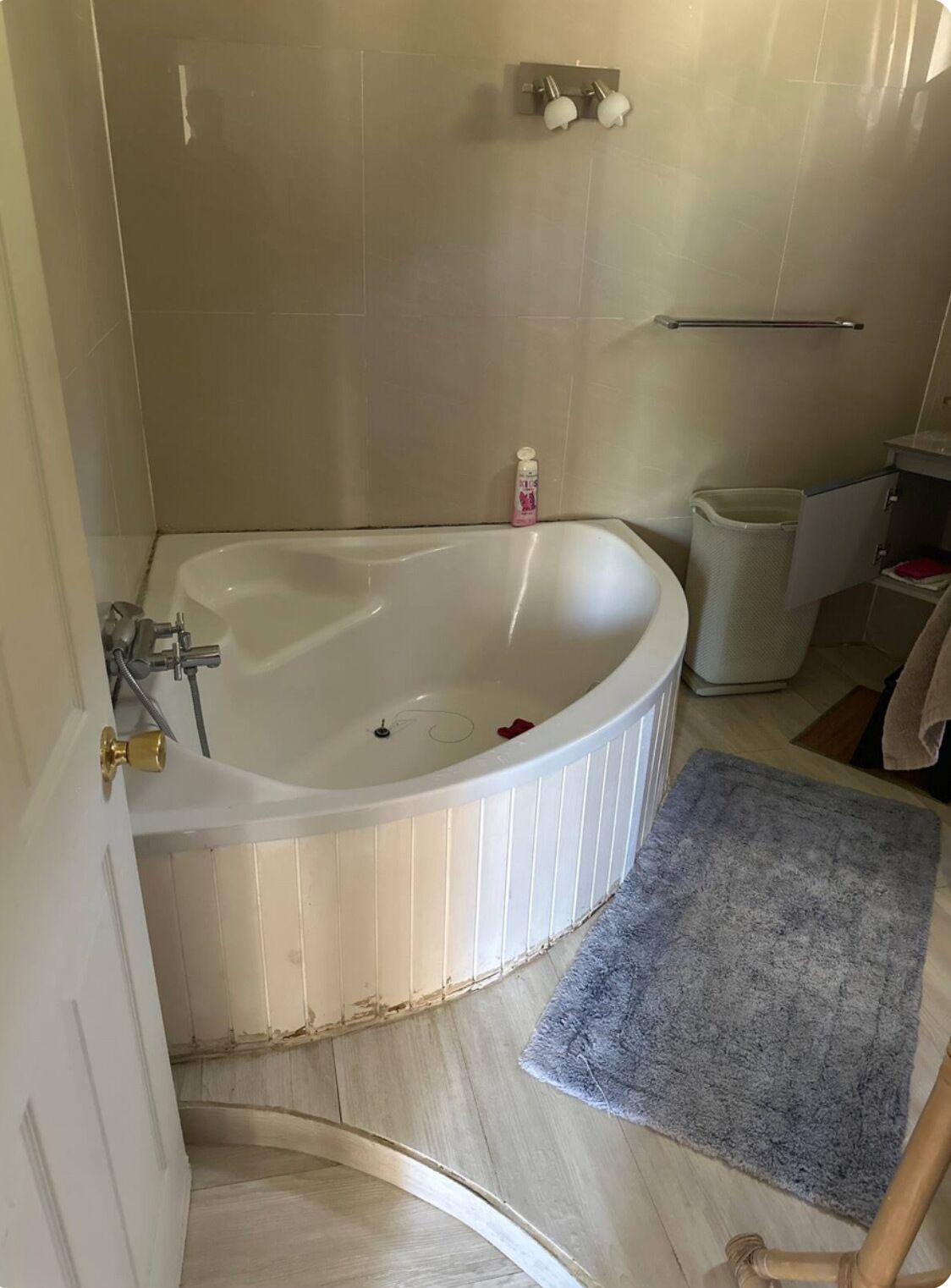 A bathroom with a freestanding bathtub, a towel rack, a trash bin, and a blue bath mat.