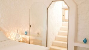 Un dormitorio con una cama, una mesita de noche y un aparador. Se ve una puerta que da a una escalera.