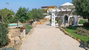 Un sendero que lleva a una zona de piscina con una estructura de piedra y un edificio con forma de cúpula.