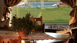 A dining table with a chess set, a potted plant, and a view of outdoor chairs and a pool. - My Rental Homes - Villa Monticchiello with pool and garden surrounding the property (Pienza)