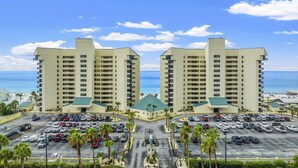 A hotel with two high-rise buildings, a parking lot, and a view of the ocean.