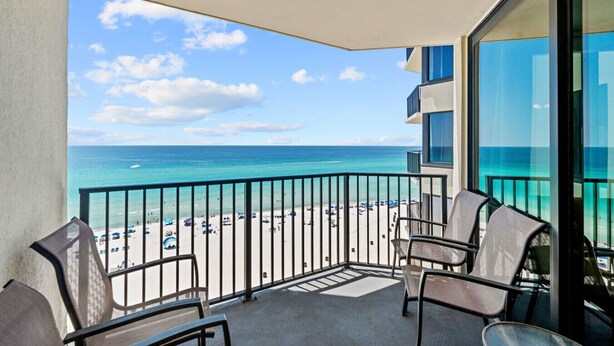 A balcony with a view of a beach and ocean. There are chairs and a table on the balcony.