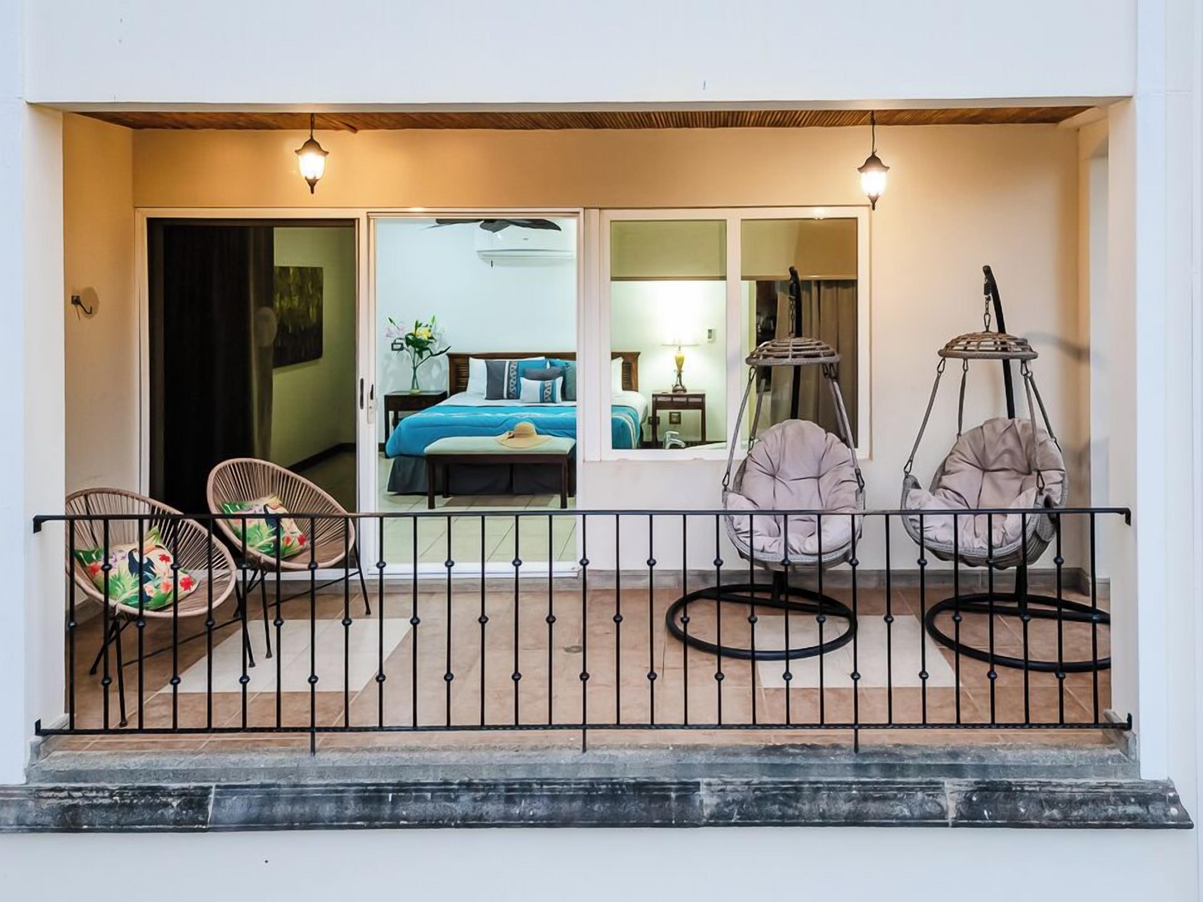 A balcony with wicker chairs, a hanging chair, and a bed visible through a glass door.
