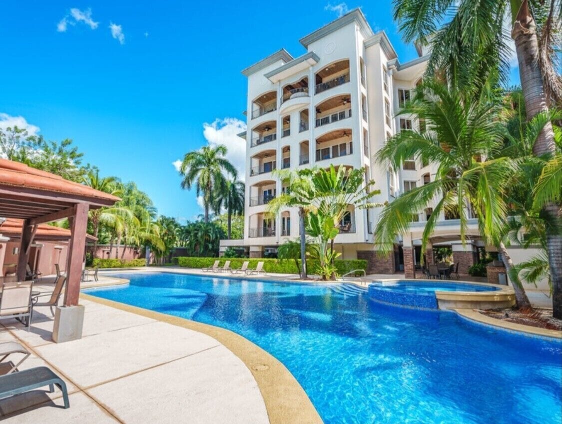Un hôtel doté d’une piscine entourée de palmiers et de chaises longues.