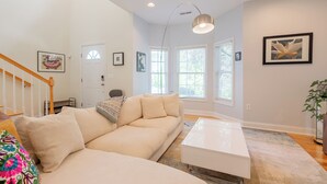 A modern living room with a beige sectional sofa, a white coffee table, and a staircase with wooden railings.