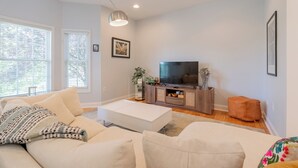 A modern living room with a large flat-screen TV, a white sofa, and a wooden entertainment unit.