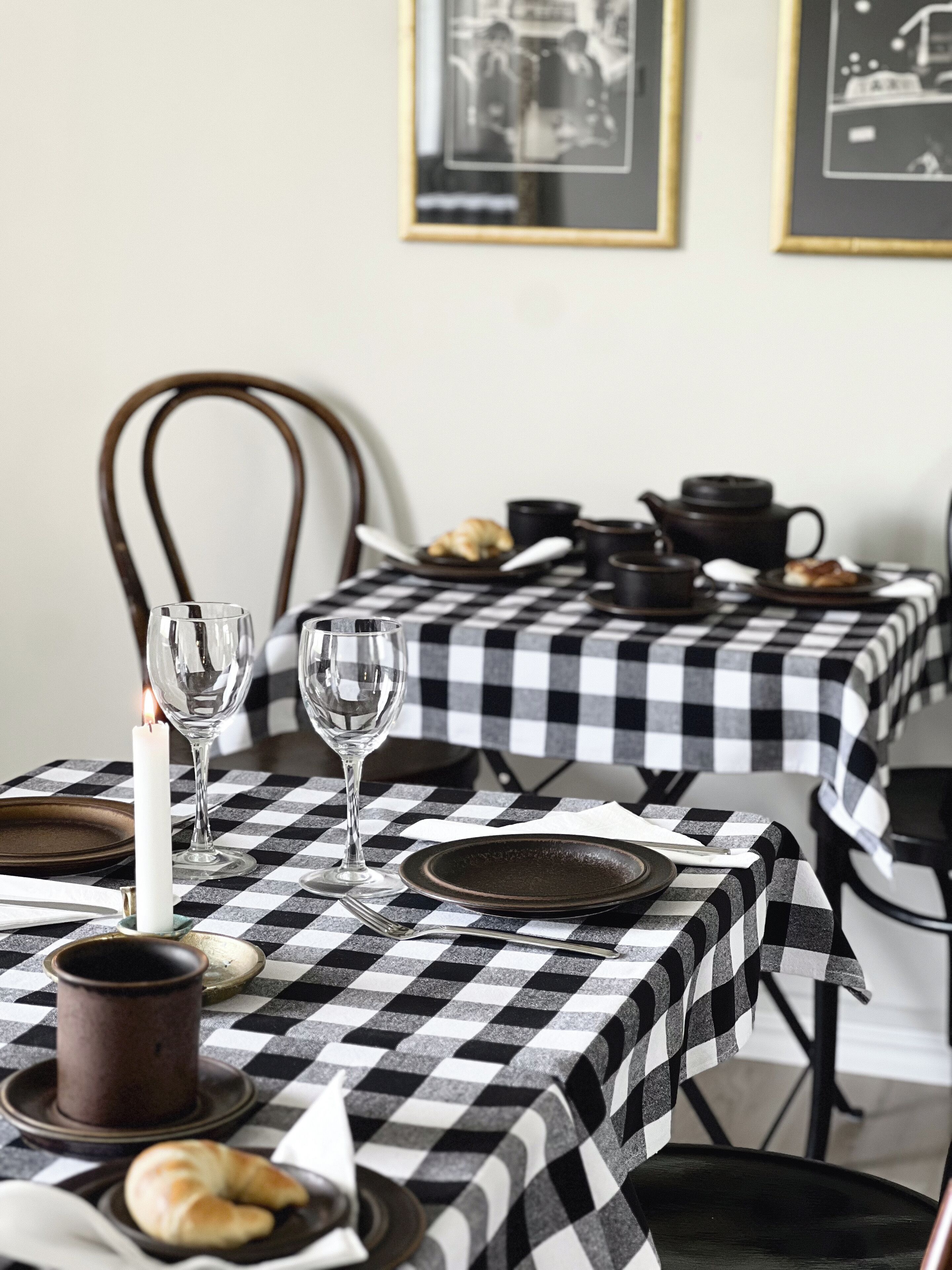 A dining table with a checkered tablecloth, a candle, wine glasses, plates, and a teapot.