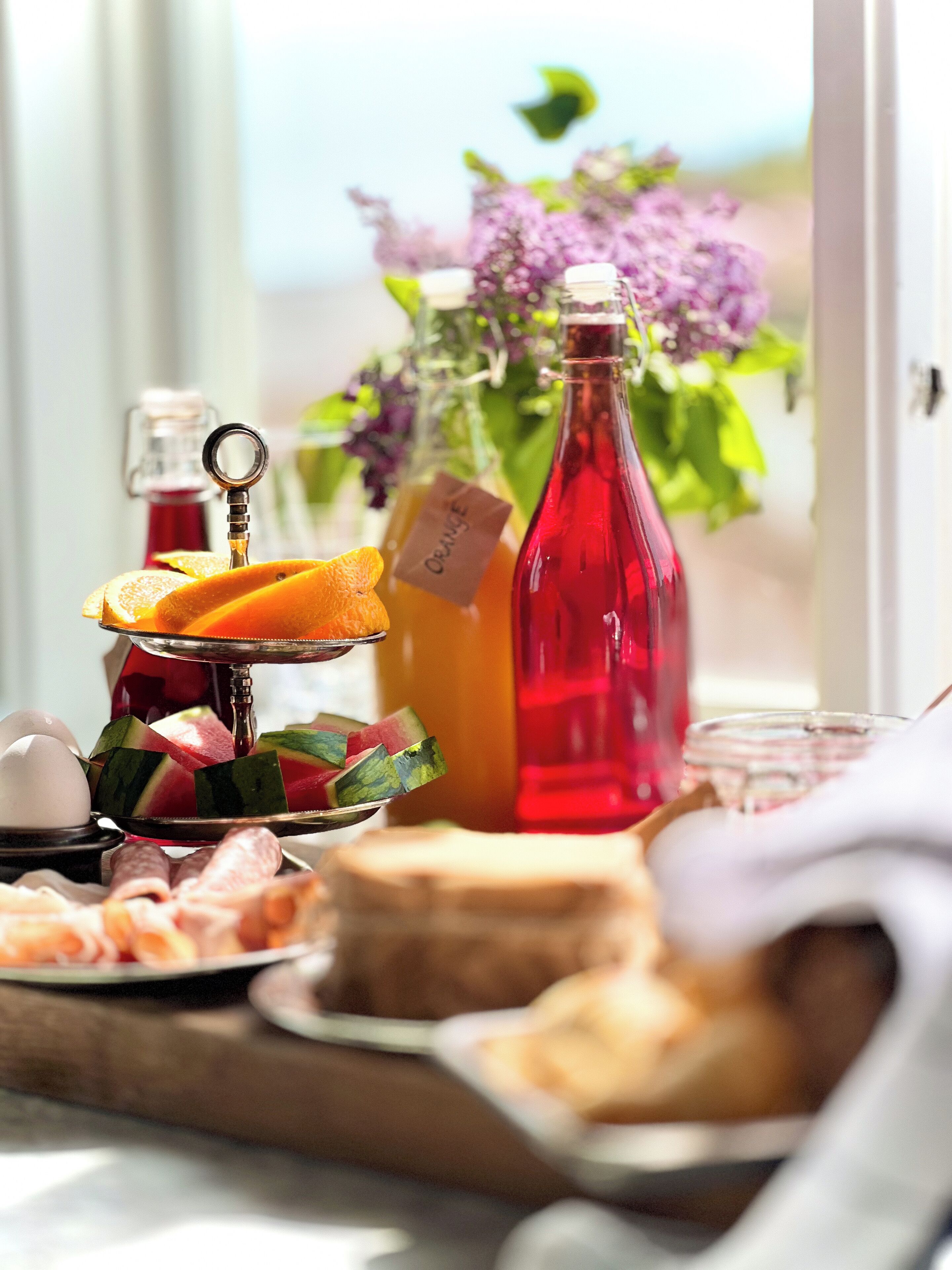A breakfast table with various food items, including sliced oranges, a bottle of orange juice, and a bottle of red juice.