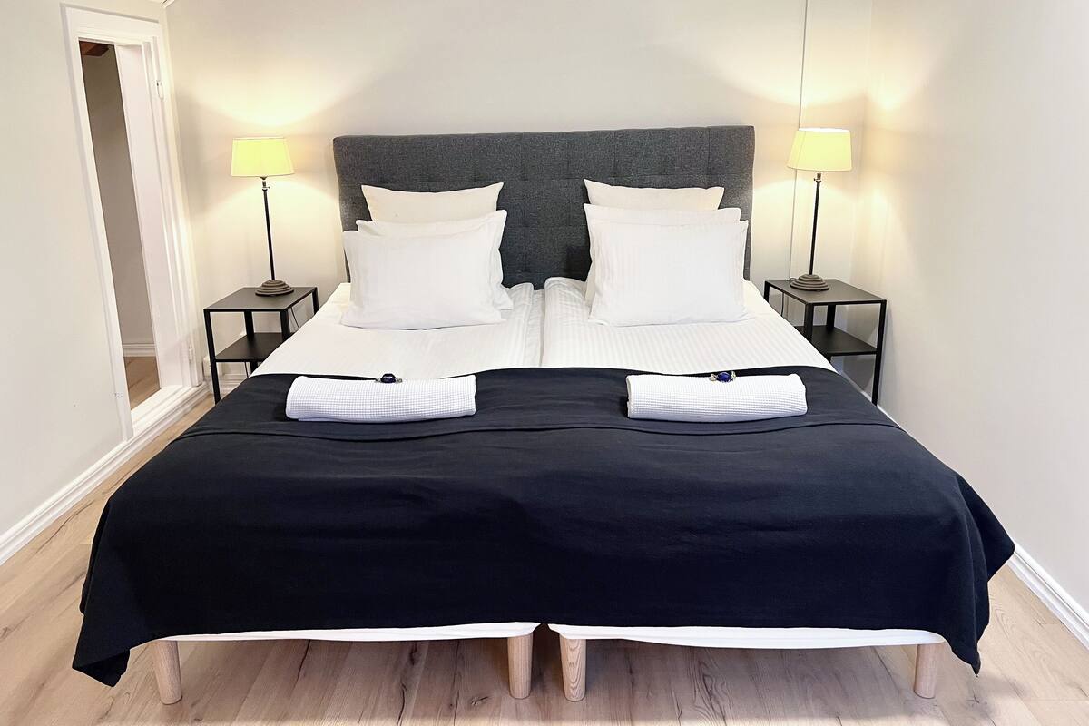 A double bed with a dark headboard, two bedside tables with lamps, and a black bedspread.
