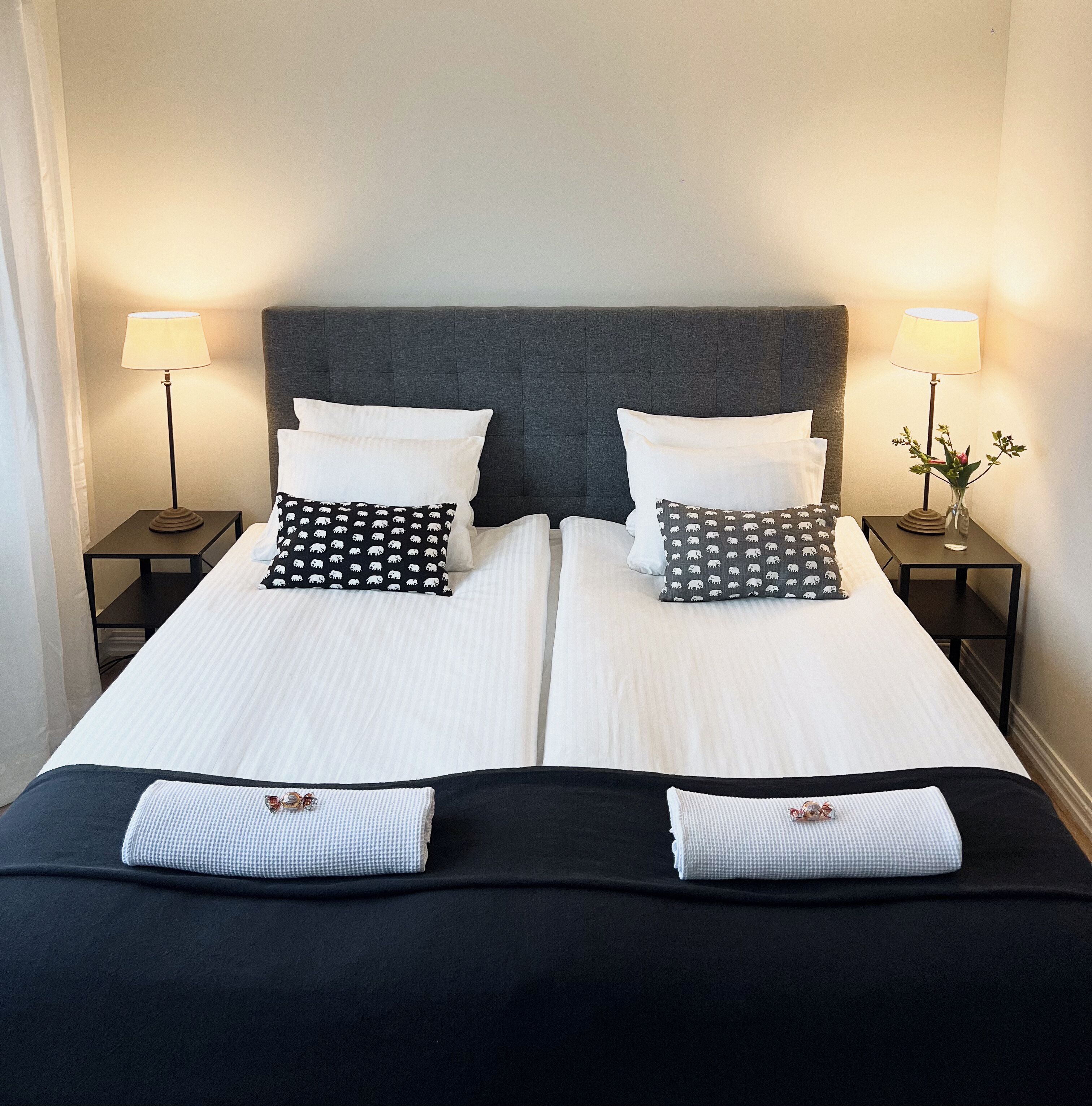 A double bed with white bedding, two black pillows with a bear pattern, and two black side tables with lamps.