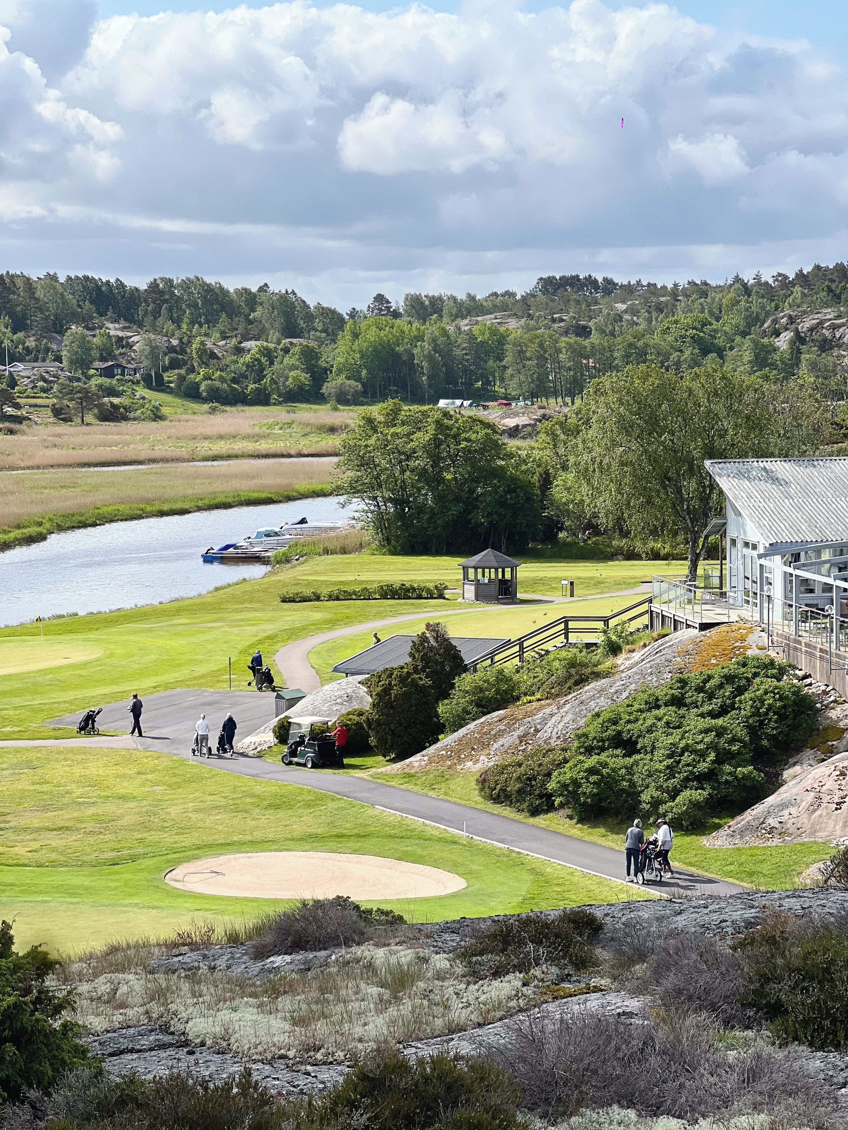 A golf course with a pond, a small pavilion, and a building with a metal roof.