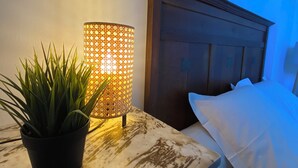 Un dormitorio con cabecera de madera, una mesita de noche con planta en maceta y una lámpara decorativa encendida.