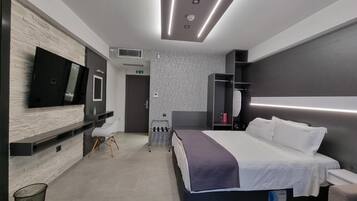 Una habitación de hotel moderna con una cama grande, un televisor de pantalla plana montado en una pared con textura, una zona de estar con una silla y una mesita.