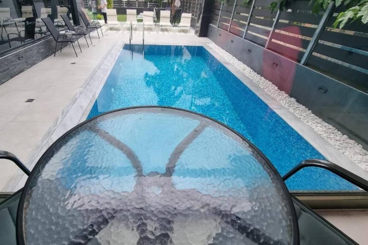 A modern indoor swimming pool with clear water, surrounded by lounge chairs and a glass balustrade.