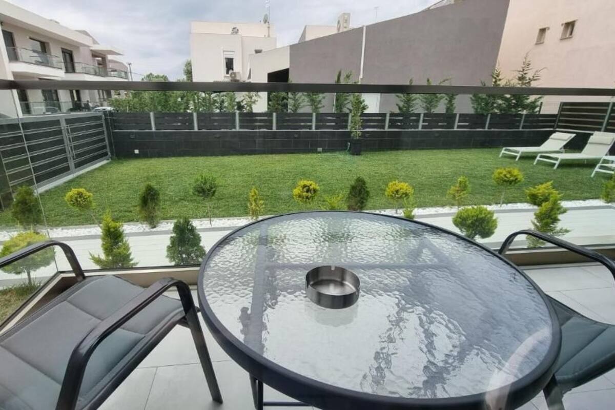A glass-top table with four chairs in a backyard with a pool, surrounded by a fence and greenery.