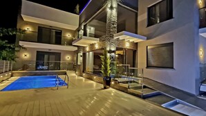 A modern two-story house with a swimming pool, outdoor lighting, and a staircase leading to the upper floor. - LUXSUITES (Pangaio)