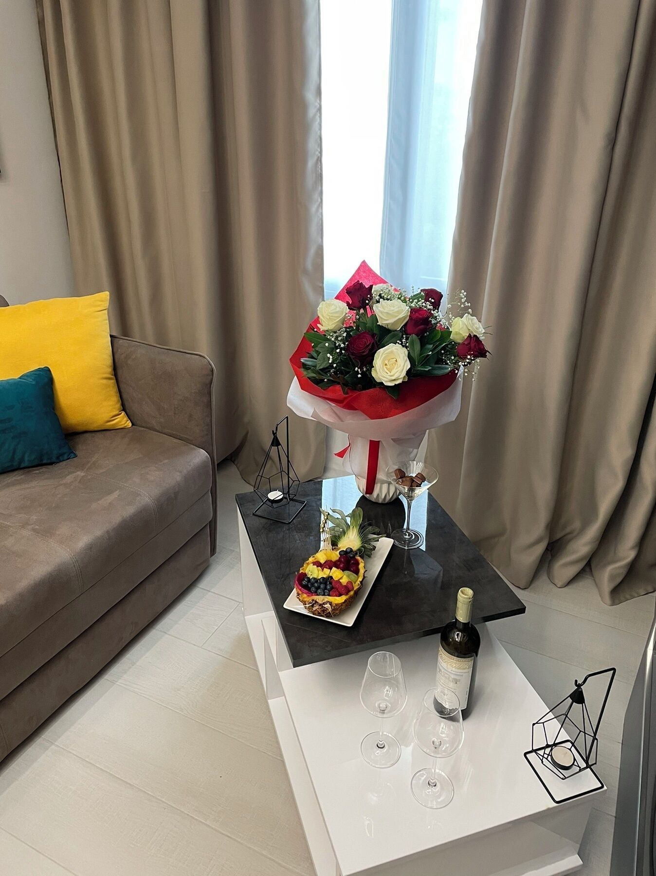 Un salon avec un canapé, une table basse sur laquelle se trouve une tarte aux fruits, une bouteille de vin et un bouquet de fleurs.