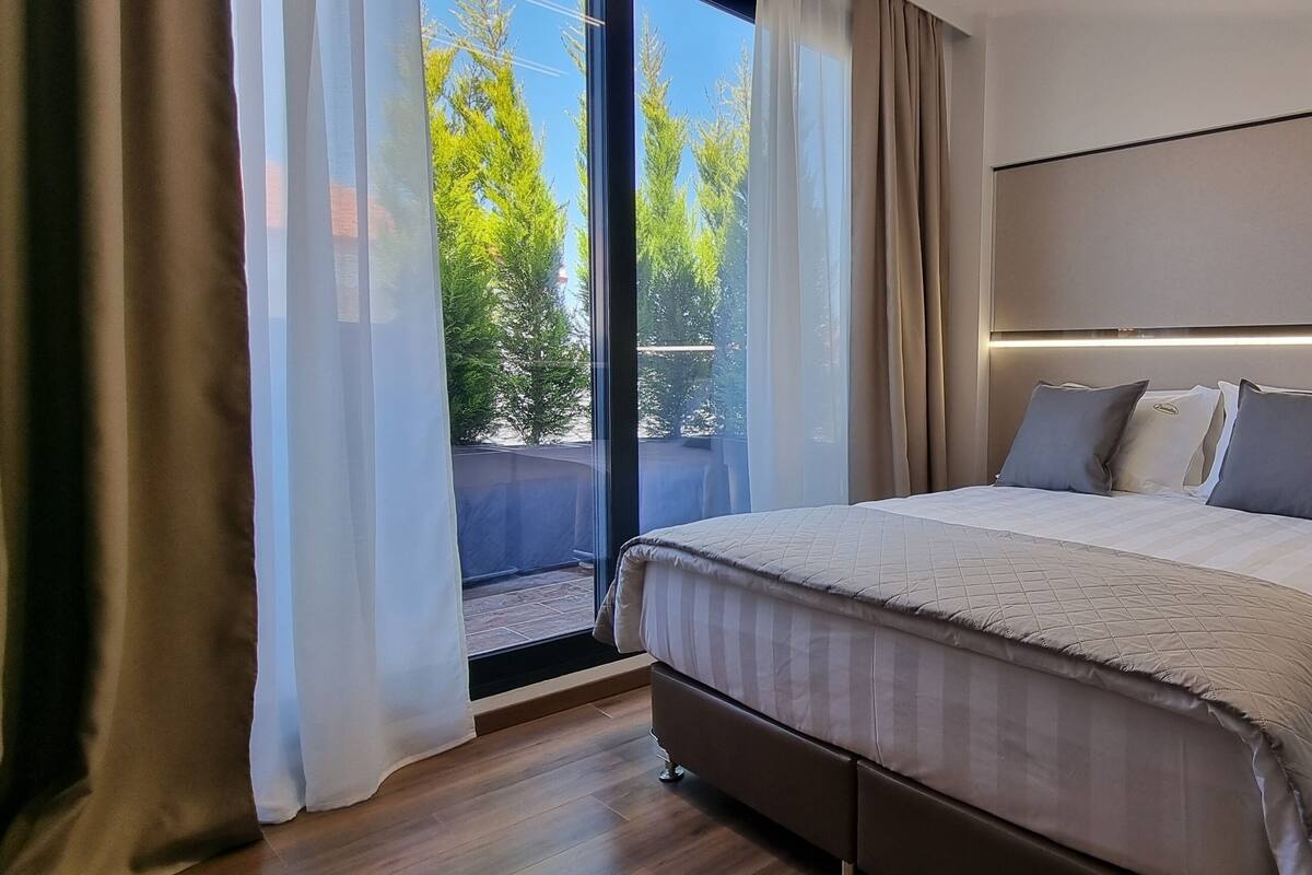A modern bedroom with a large bed, a glass door leading to a balcony, and a minimalist design.