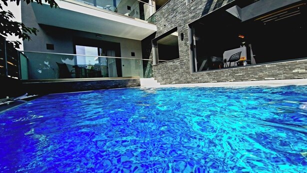 A modern pool area with clear blue water, surrounded by a contemporary building with large windows and a stone facade. - LUXSUITES (Pangaio)