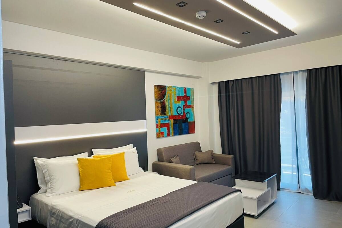 A modern hotel room with a large bed, a sofa, a painting on the wall, and a view of the outside through the window.