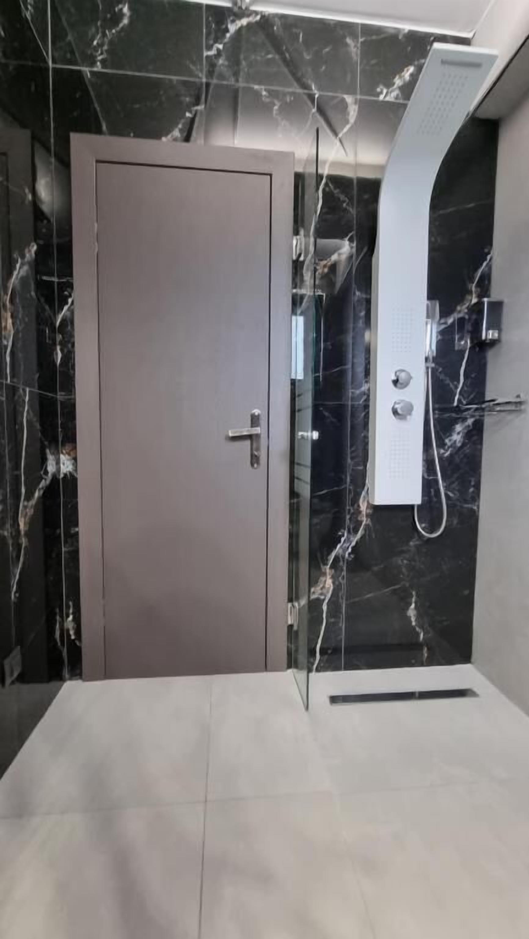 Ein modernes Badezimmer mit Marmorwand, einer Dusche und einer Tür.