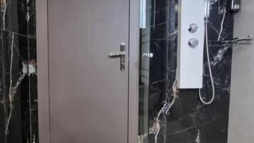 Ein modernes Badezimmer mit Marmorwand, einer Dusche und einer Tür.